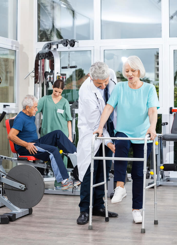 Older male and female at rehab gym with professional guiding them through exercises